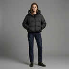 Person wearing a black puffer jacket and dark jeans on a gray background