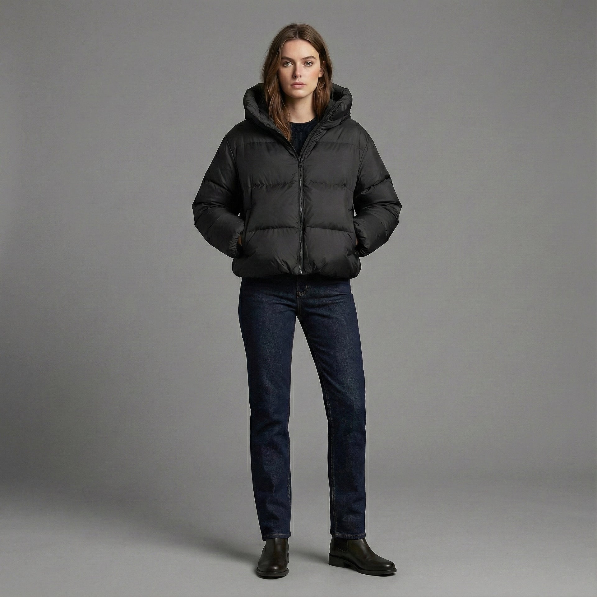 Person wearing a black puffer jacket and dark jeans on a gray background