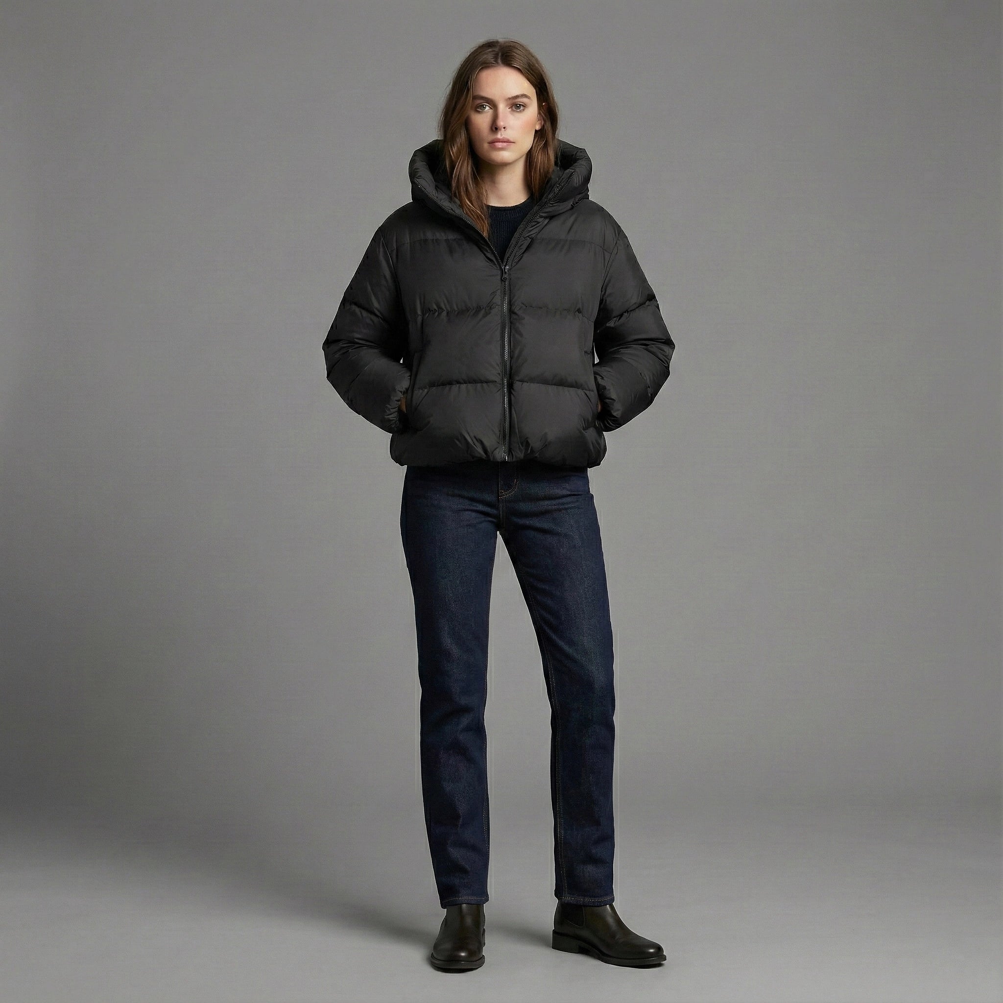 Person wearing a black puffer jacket and dark jeans on a gray background
