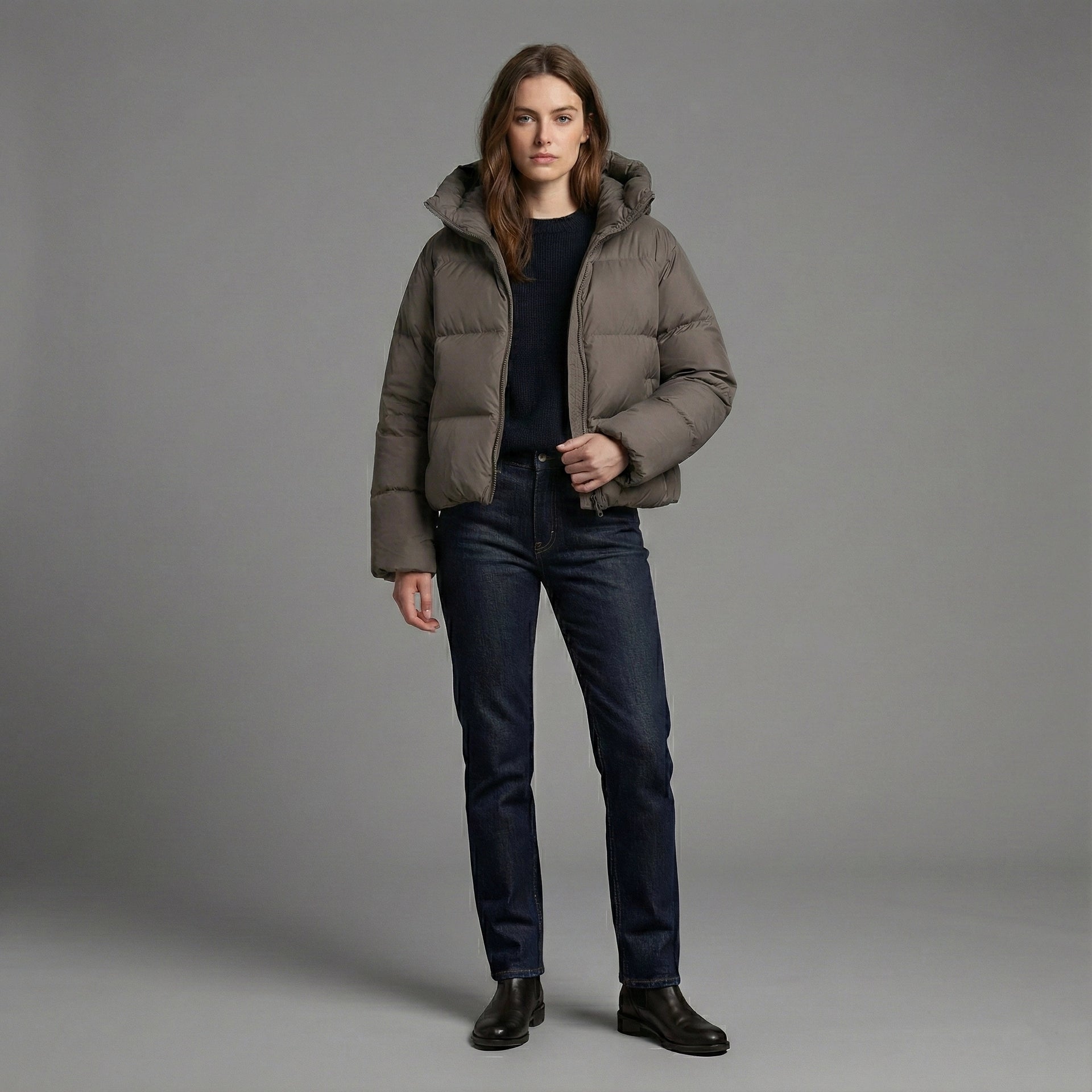 Person wearing a brown puffer jacket and dark jeans on a gray background
