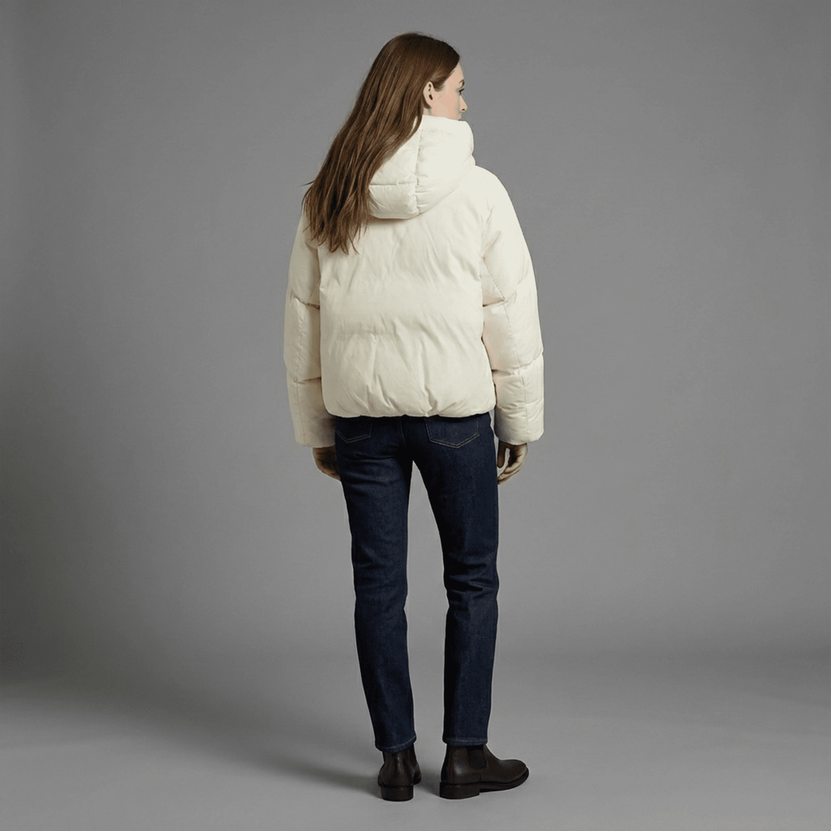 Person wearing a white puffer jacket and dark jeans on a gray background