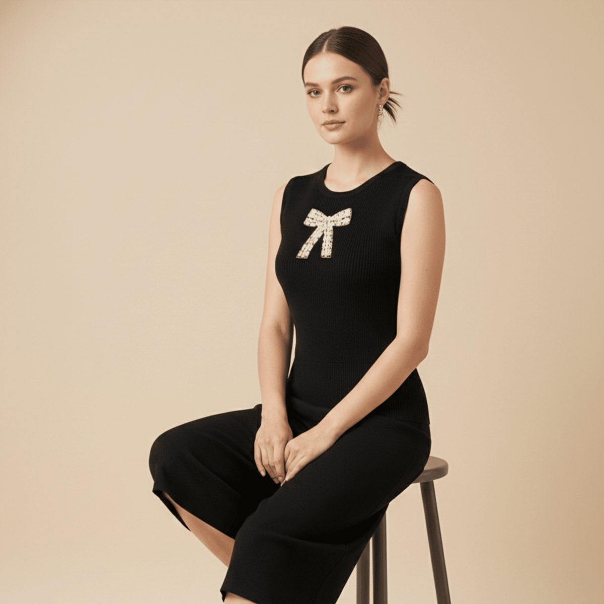 Woman wearing a black sleeveless top with a bow design, sitting on a beige background