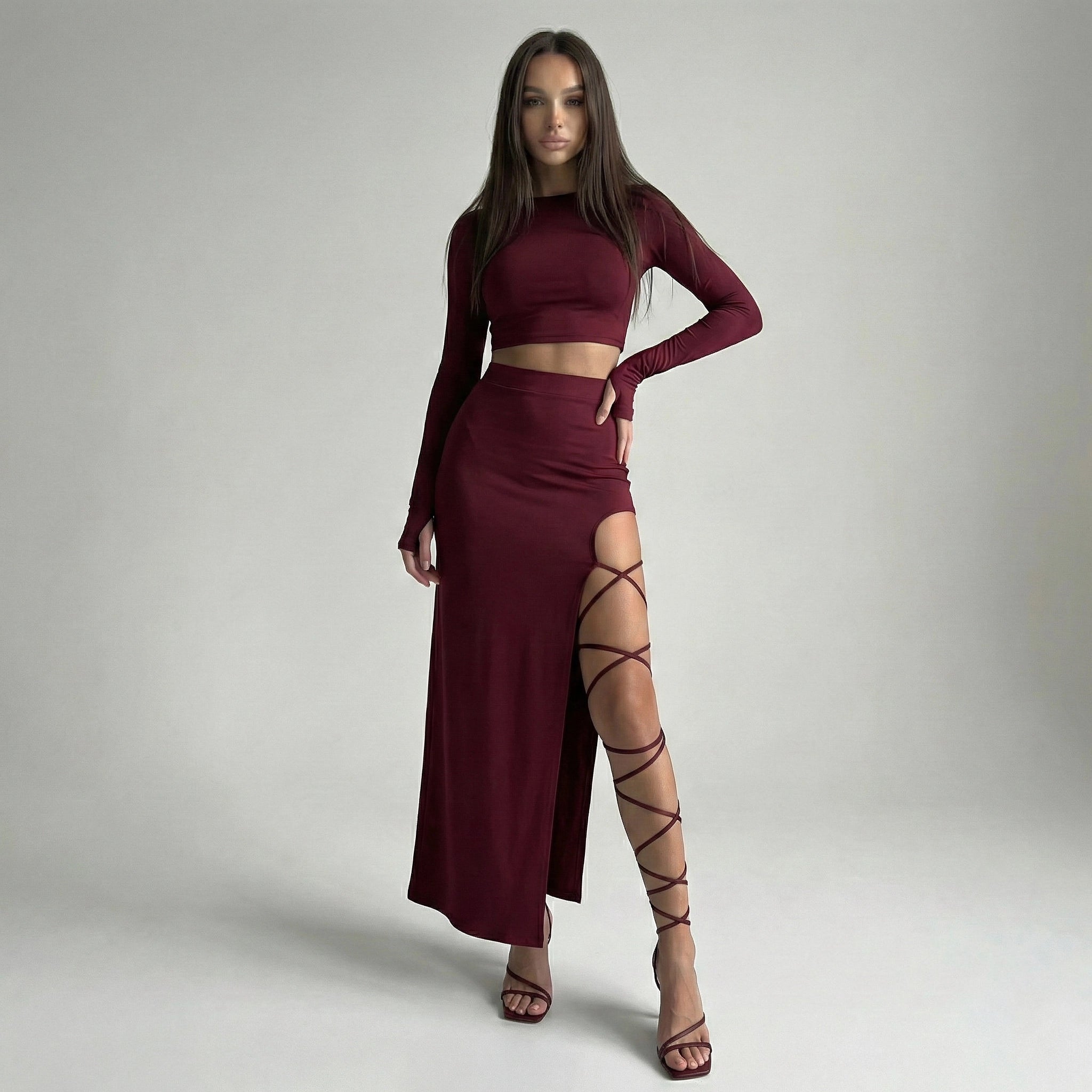Woman wearing a burgundy outfit with a high slit skirt on a gray background