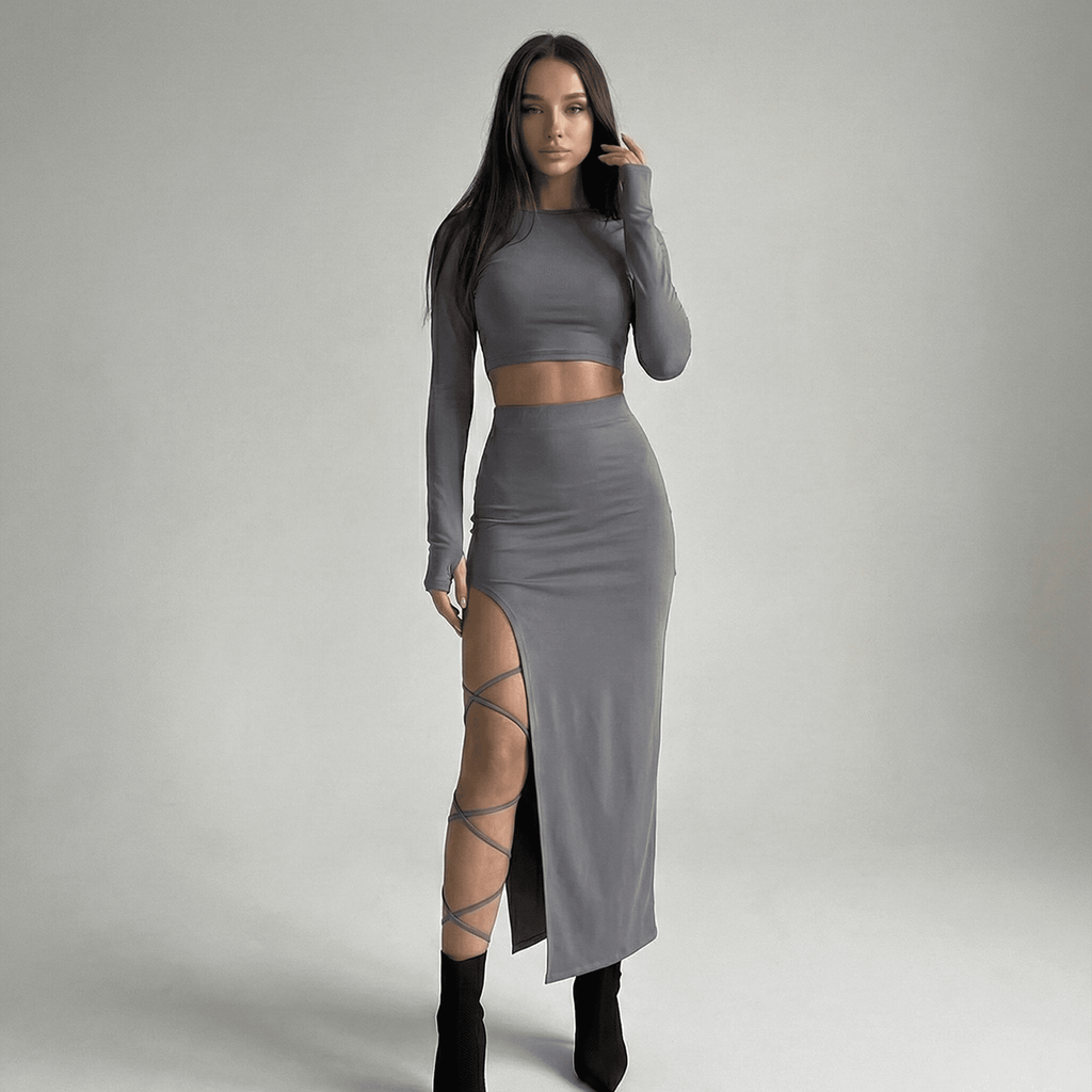 Woman wearing a gray long-sleeve top and skirt with a high slit on a plain background