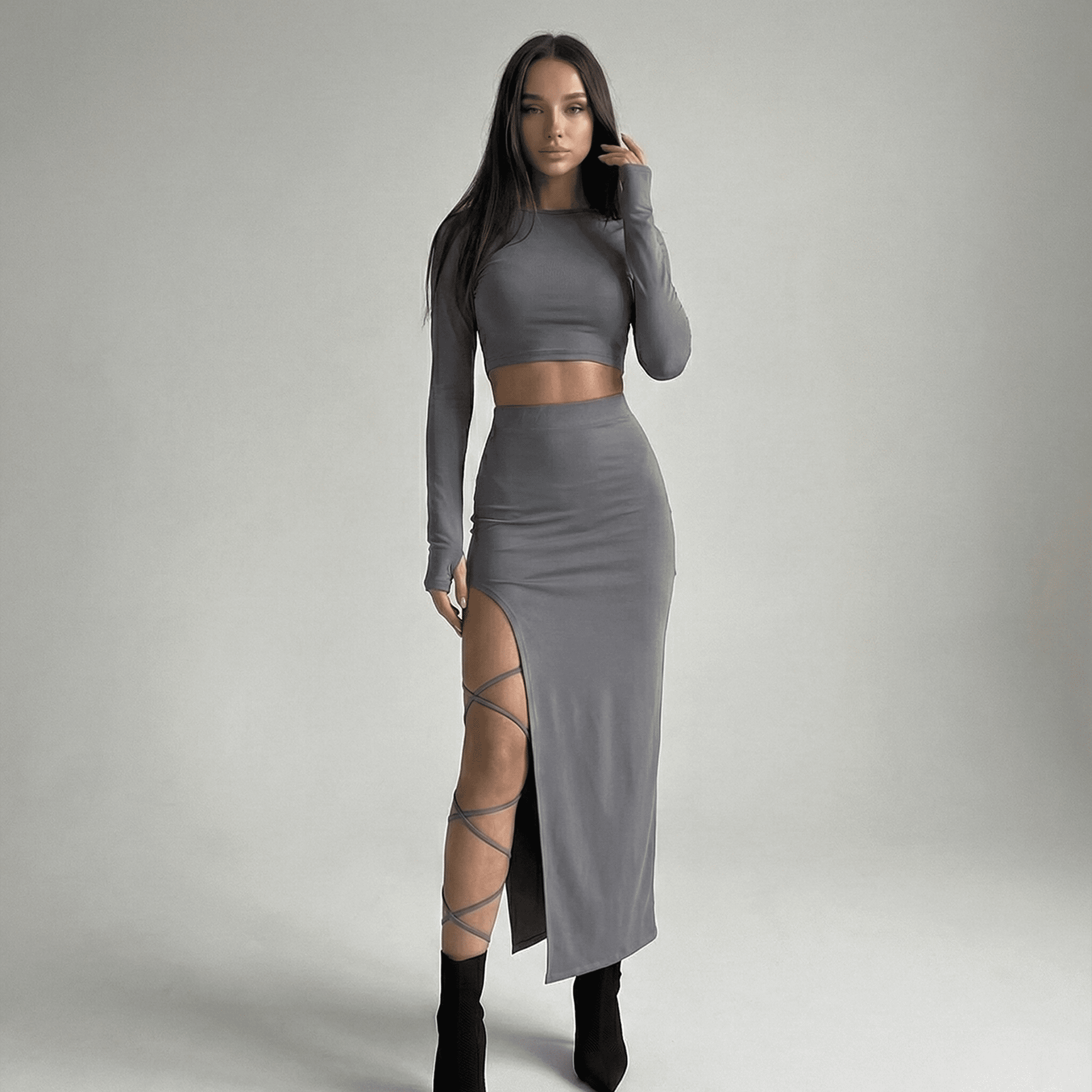 Woman wearing a gray long-sleeve top and skirt with a high slit on a plain background