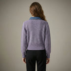 Person wearing a purple sweater with a blue collar against a neutral background