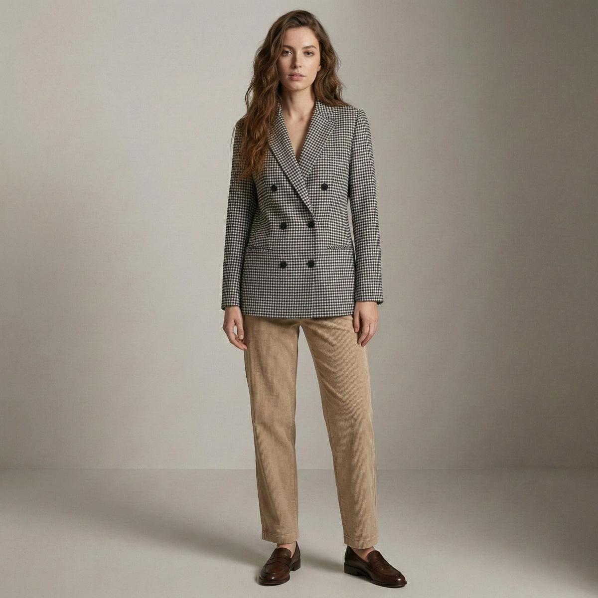 Woman wearing a checkered blazer and beige pants against a plain background