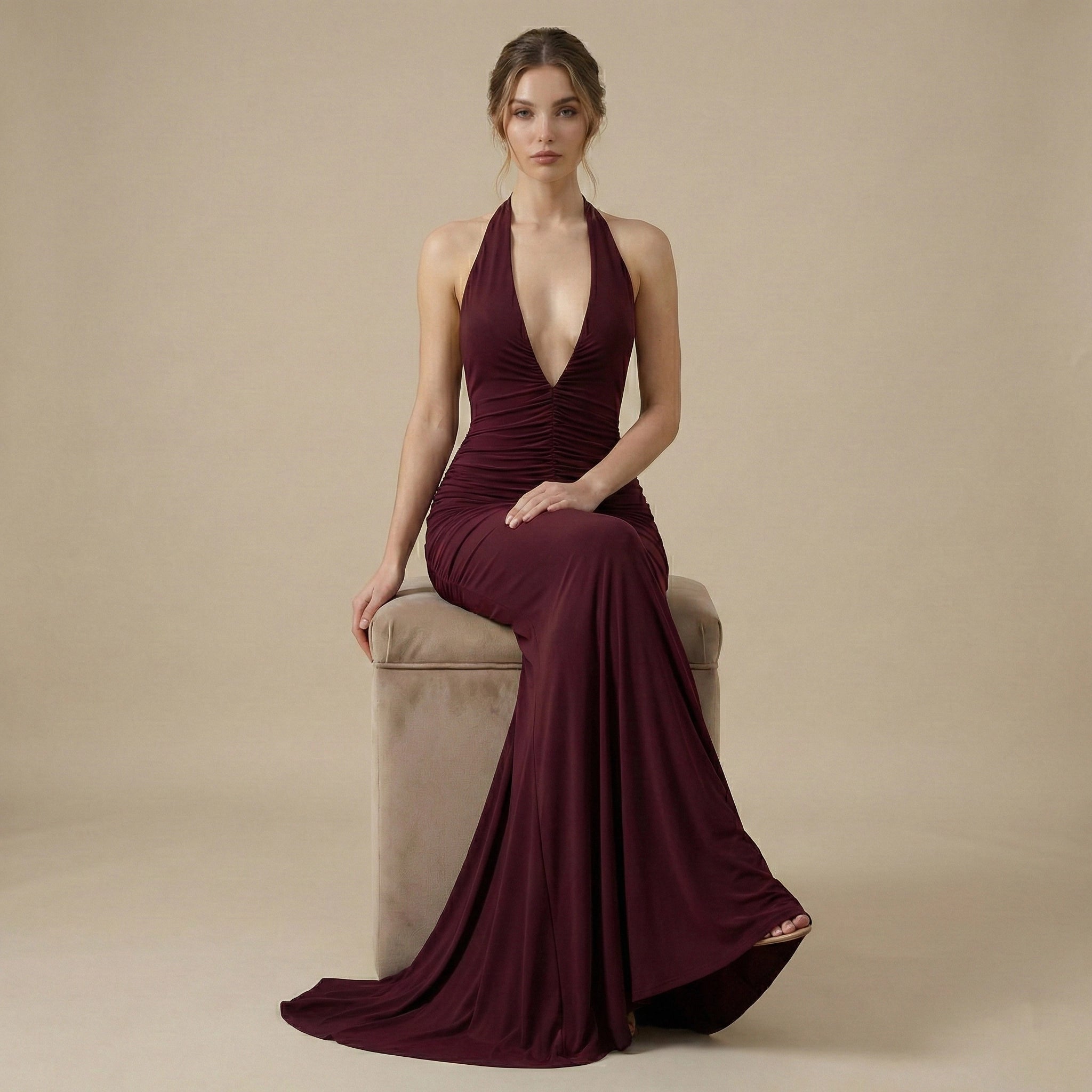 Woman in a burgundy evening gown sitting on a beige chair against a beige background