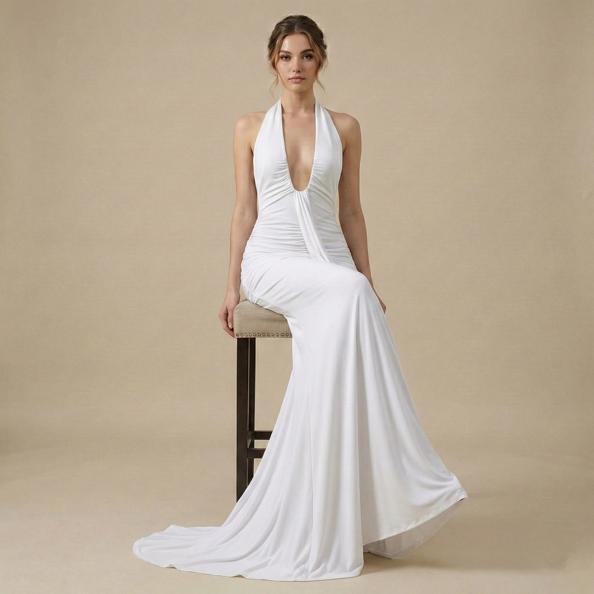 Woman wearing a white halter neck gown sitting on a chair against a beige background