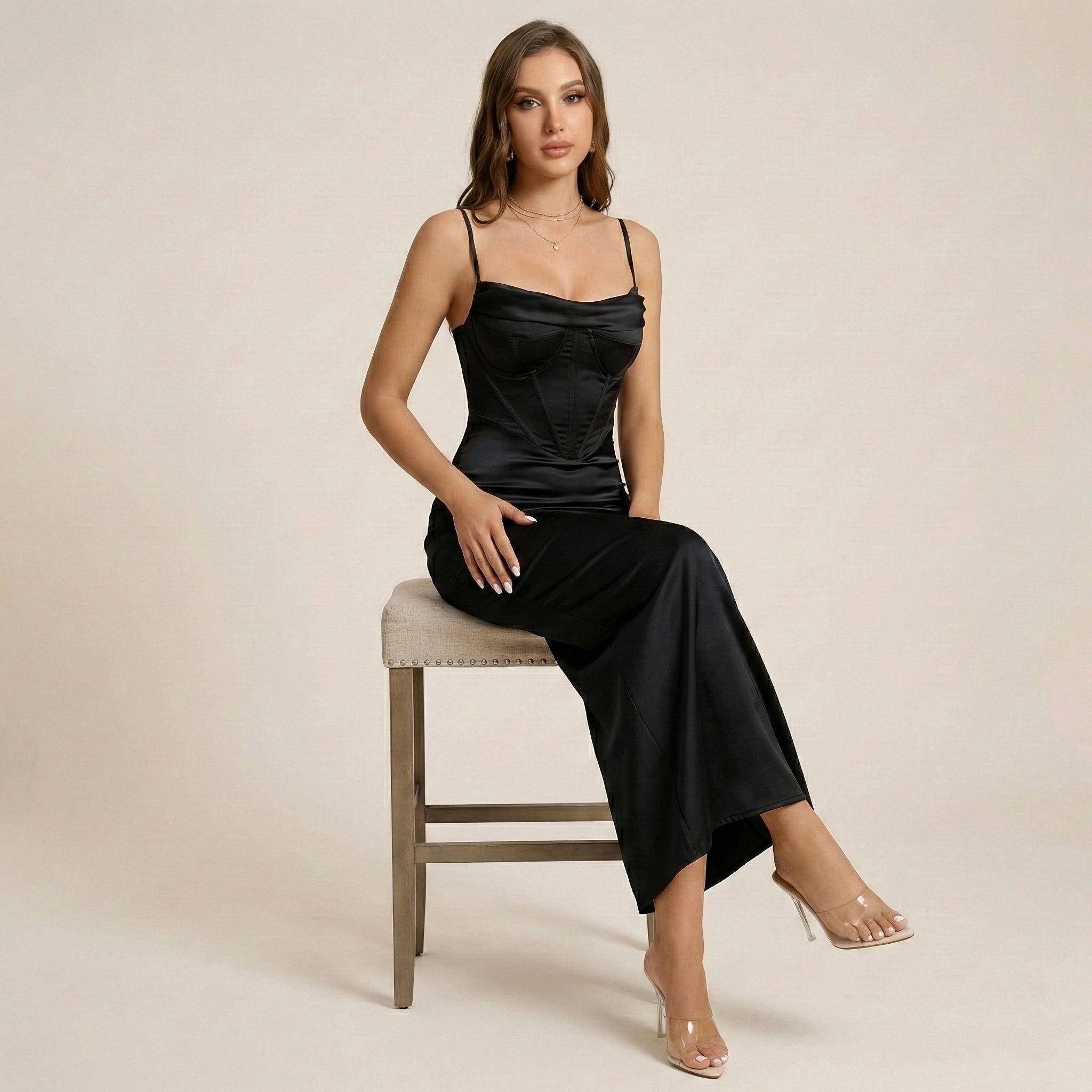 Woman in a black dress sitting on a chair against a beige background