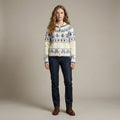 Woman wearing a patterned sweater and dark jeans against a plain background