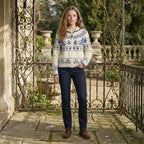 Woman wearing a patterned sweater and dark jeans standing on a stone path with decorative railing.