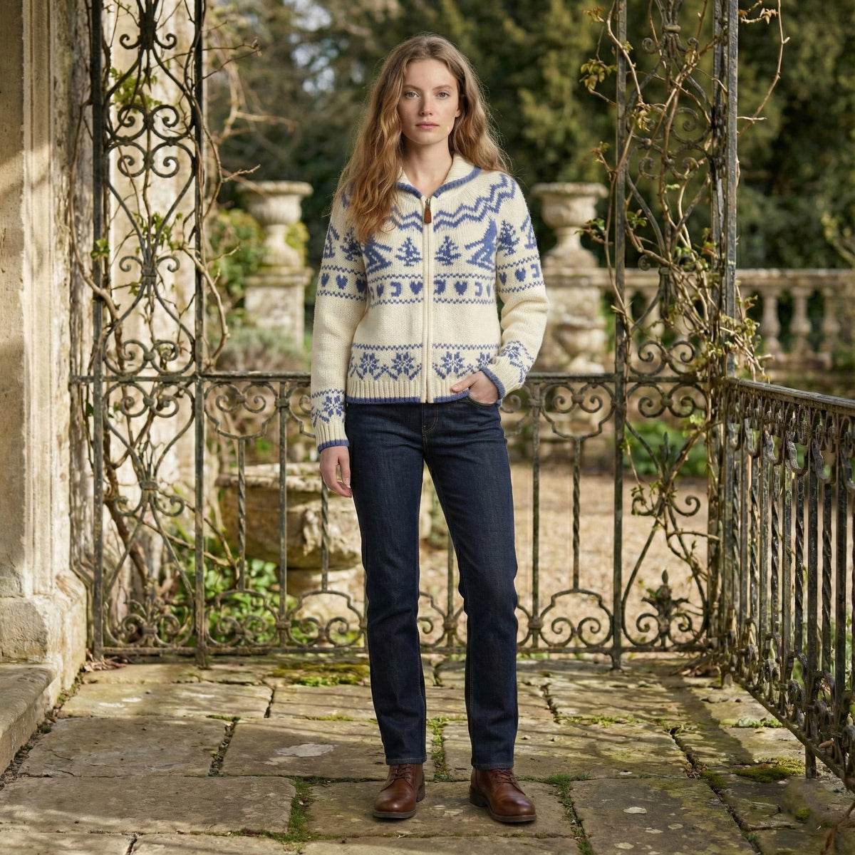 Woman wearing a patterned sweater and dark jeans standing on a stone path with decorative railing.