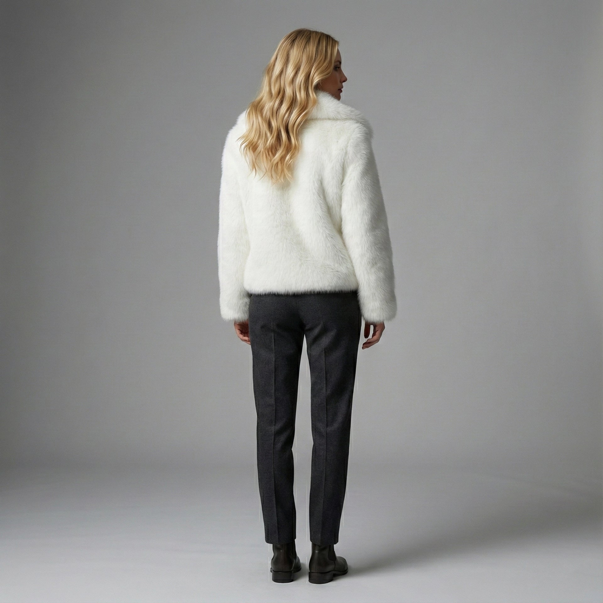 Person wearing a white fluffy sweater and dark pants against a gray background