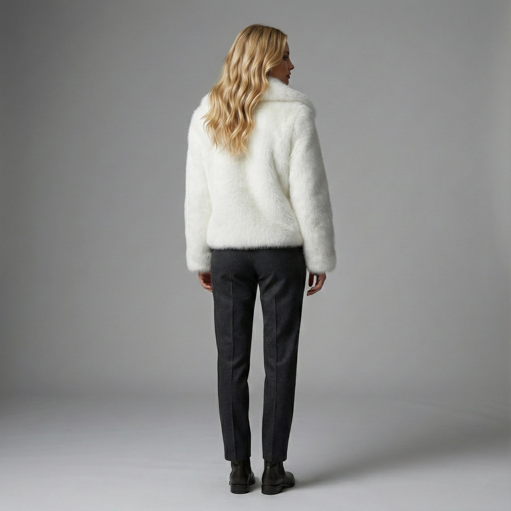 Person wearing a white fluffy sweater and dark pants against a gray background