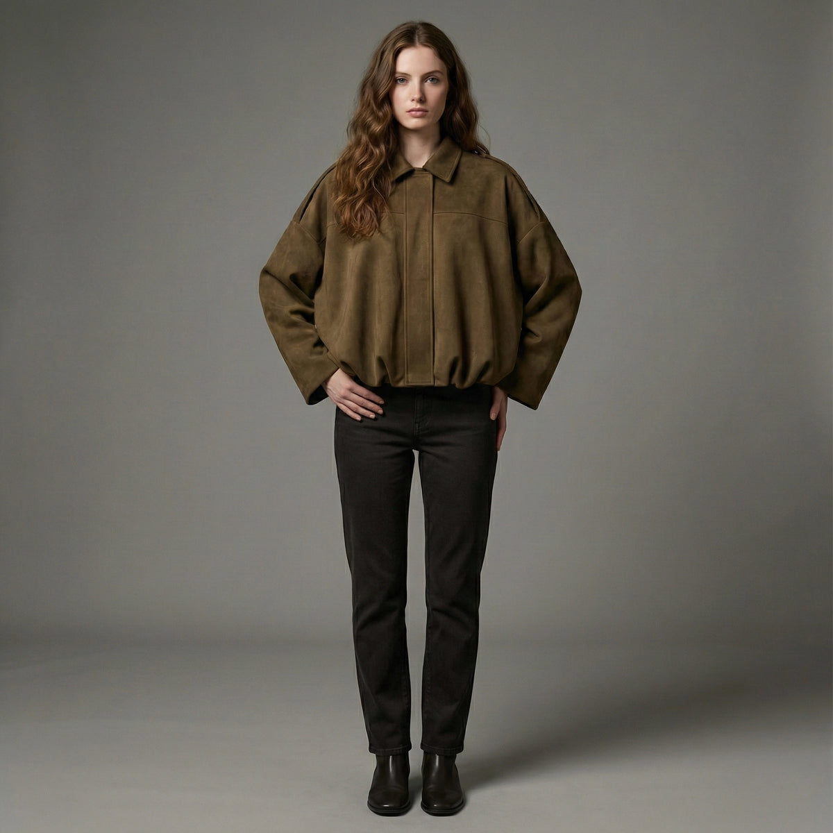 Woman wearing a brown jacket and black pants against a gray background