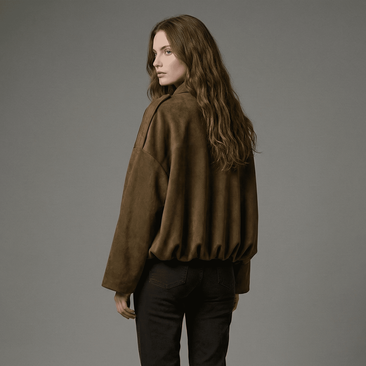 Woman wearing a brown jacket and black pants against a gray background