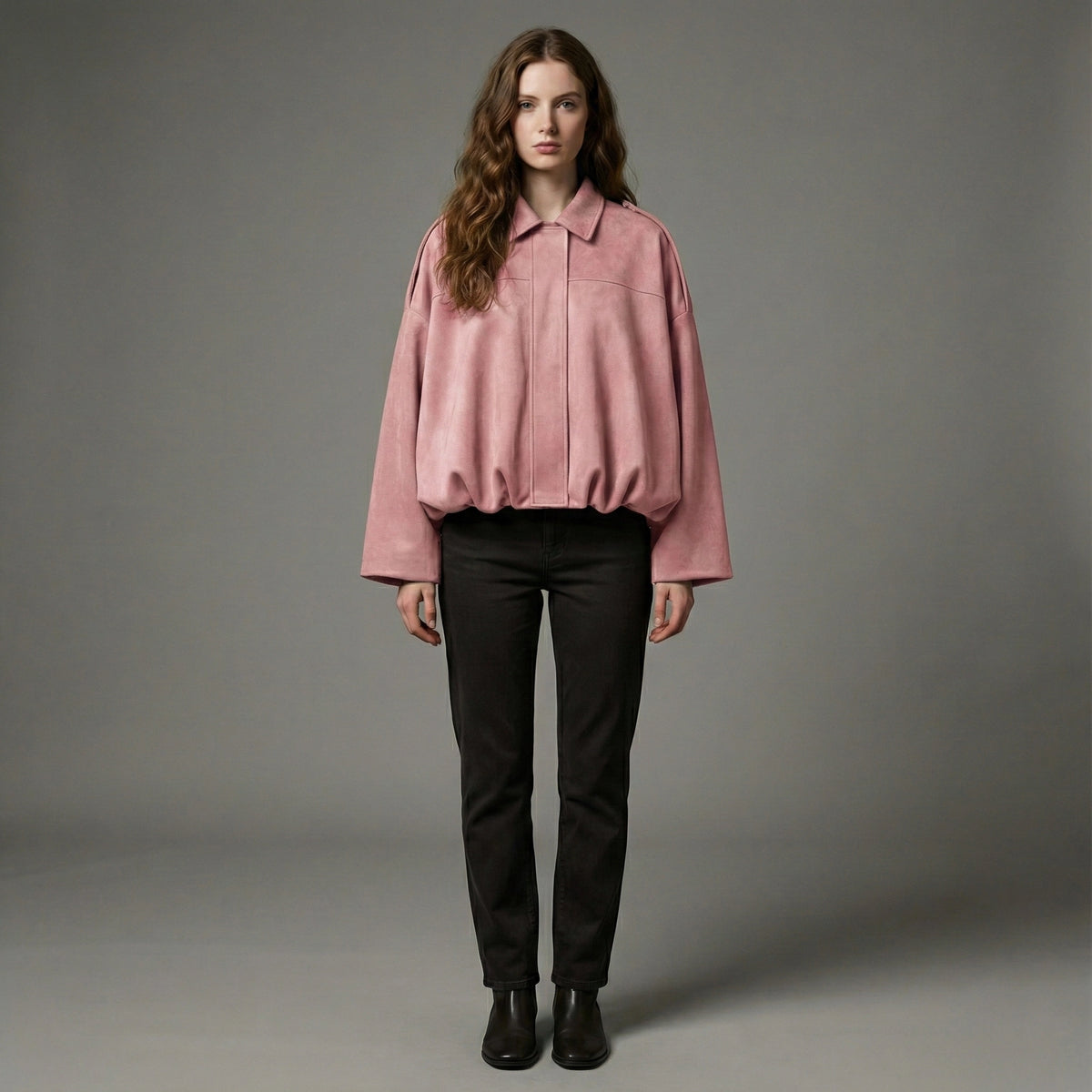 Woman wearing a pink shirt and black pants against a gray background