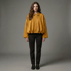 Woman wearing a mustard yellow jacket and black pants against a gray background
