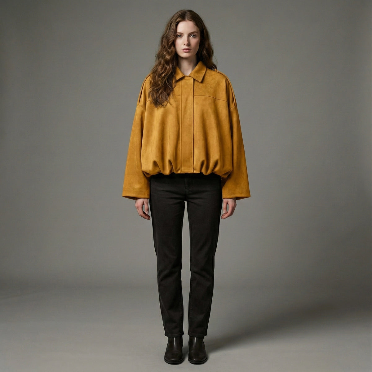 Woman wearing a mustard yellow jacket and black pants against a gray background