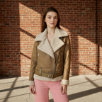 Woman wearing a brown leather jacket with white fur lining against a brick wall.