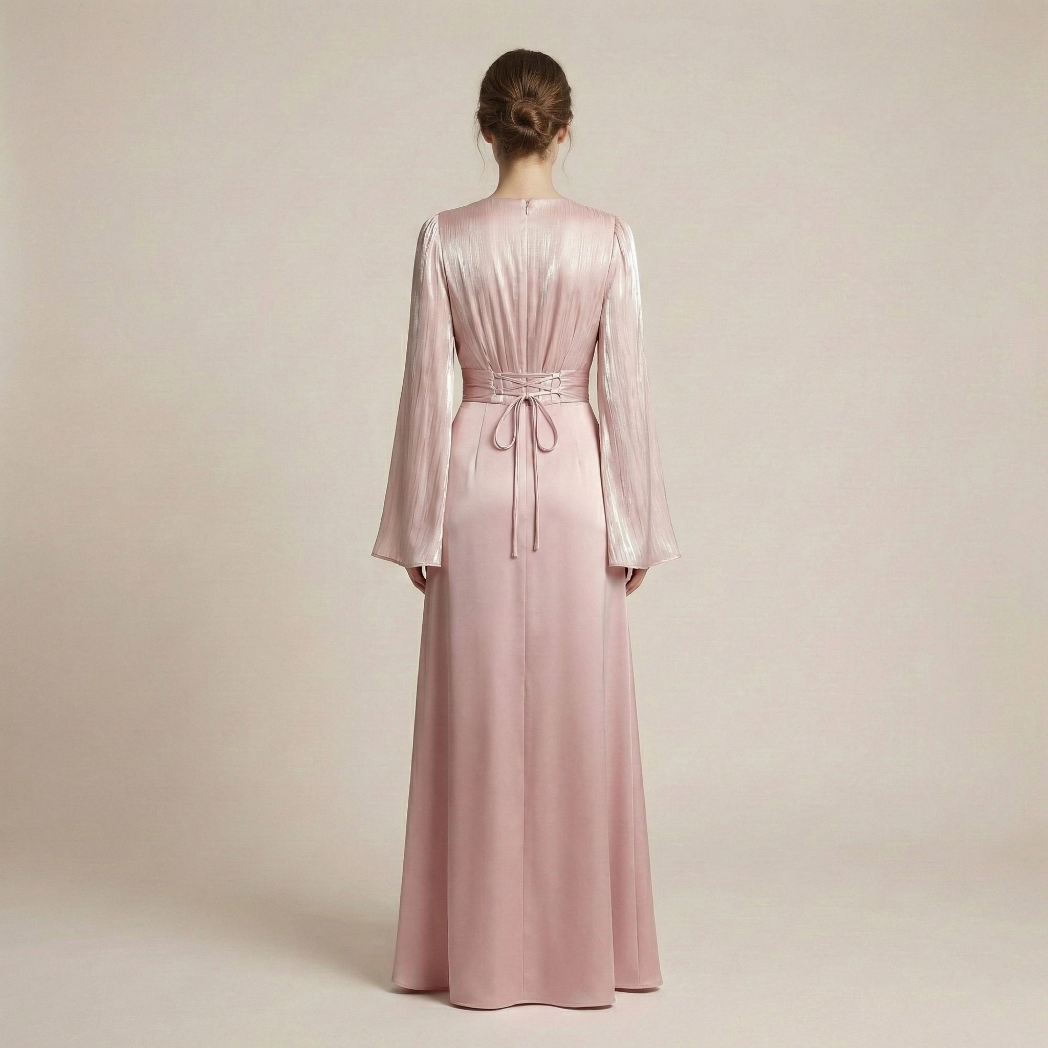 Woman wearing a long pink dress with sheer sleeves on a beige background