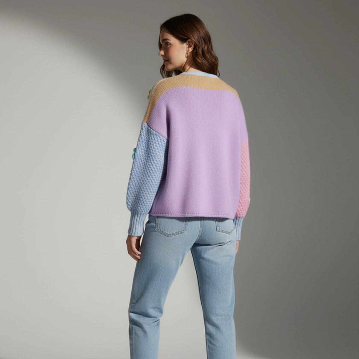 Woman wearing a pastel sweater and light blue jeans against a gray background
