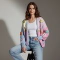 Woman wearing a colorful cardigan with floral patterns sitting on a stool against a plain background