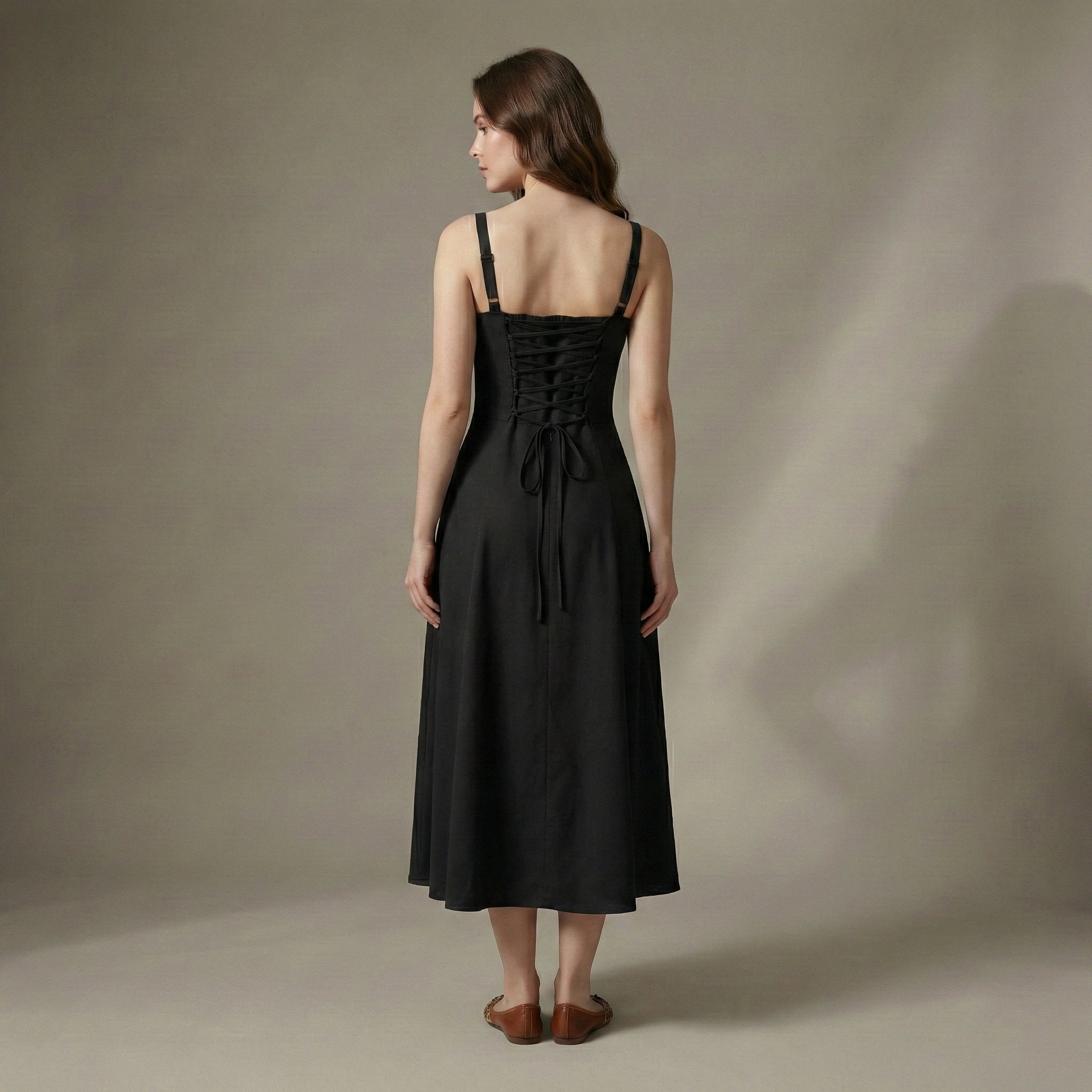 Woman wearing a black dress with a lace-up back against a neutral background