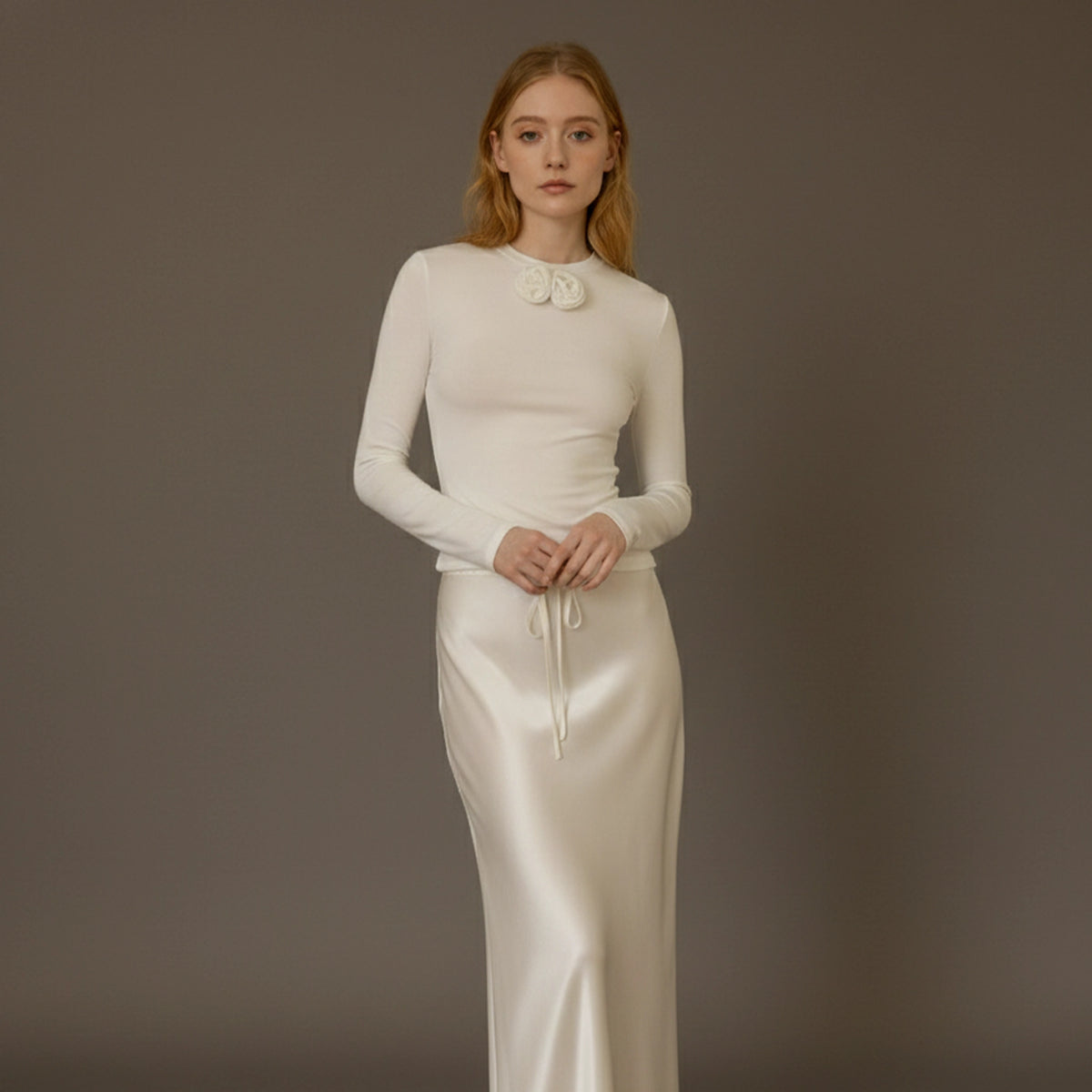 Woman wearing a white long-sleeve top and skirt set against a brown background