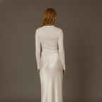 Woman wearing a long, light-colored dress against a plain background