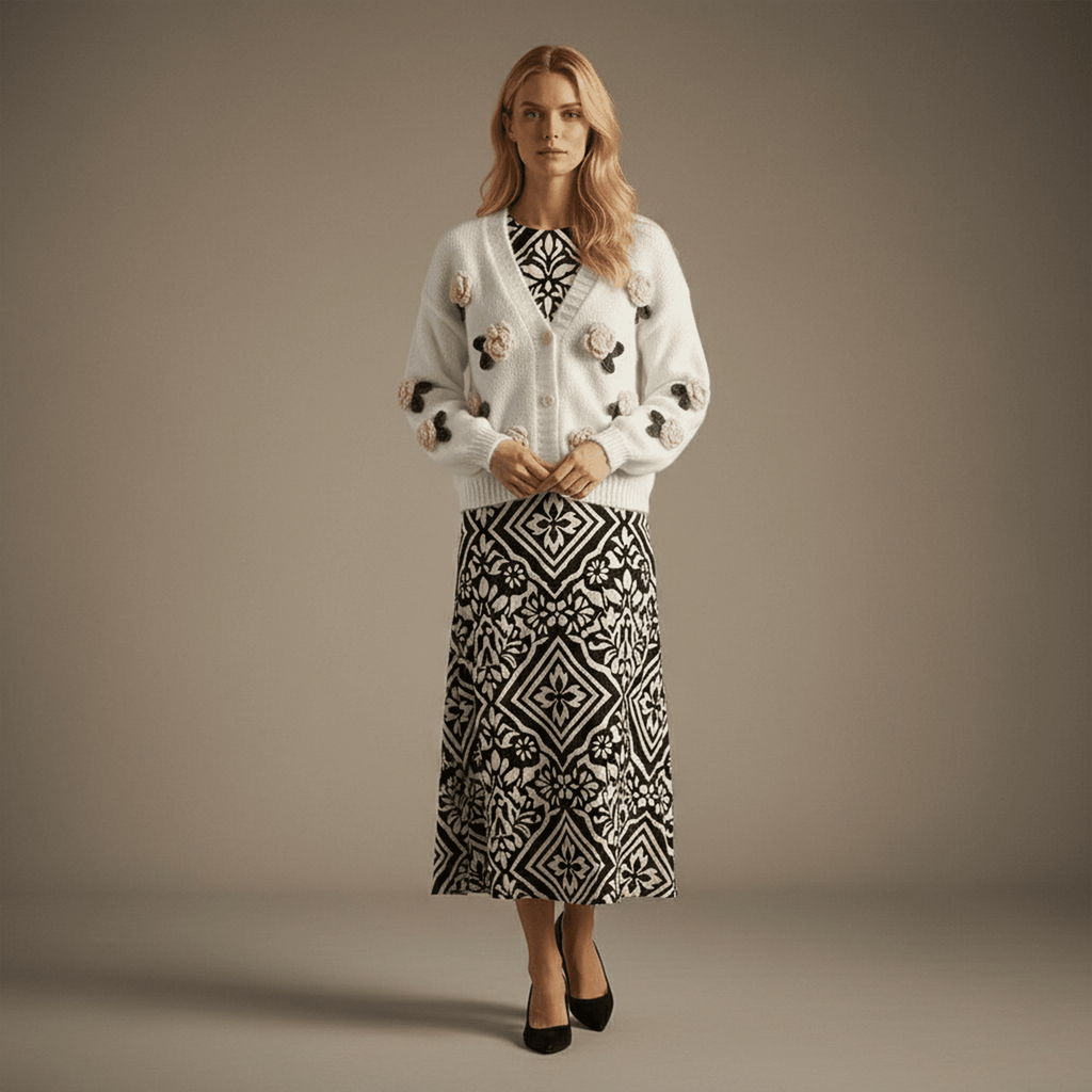 Woman wearing a white cardigan with floral embellishments and a patterned skirt on a beige background