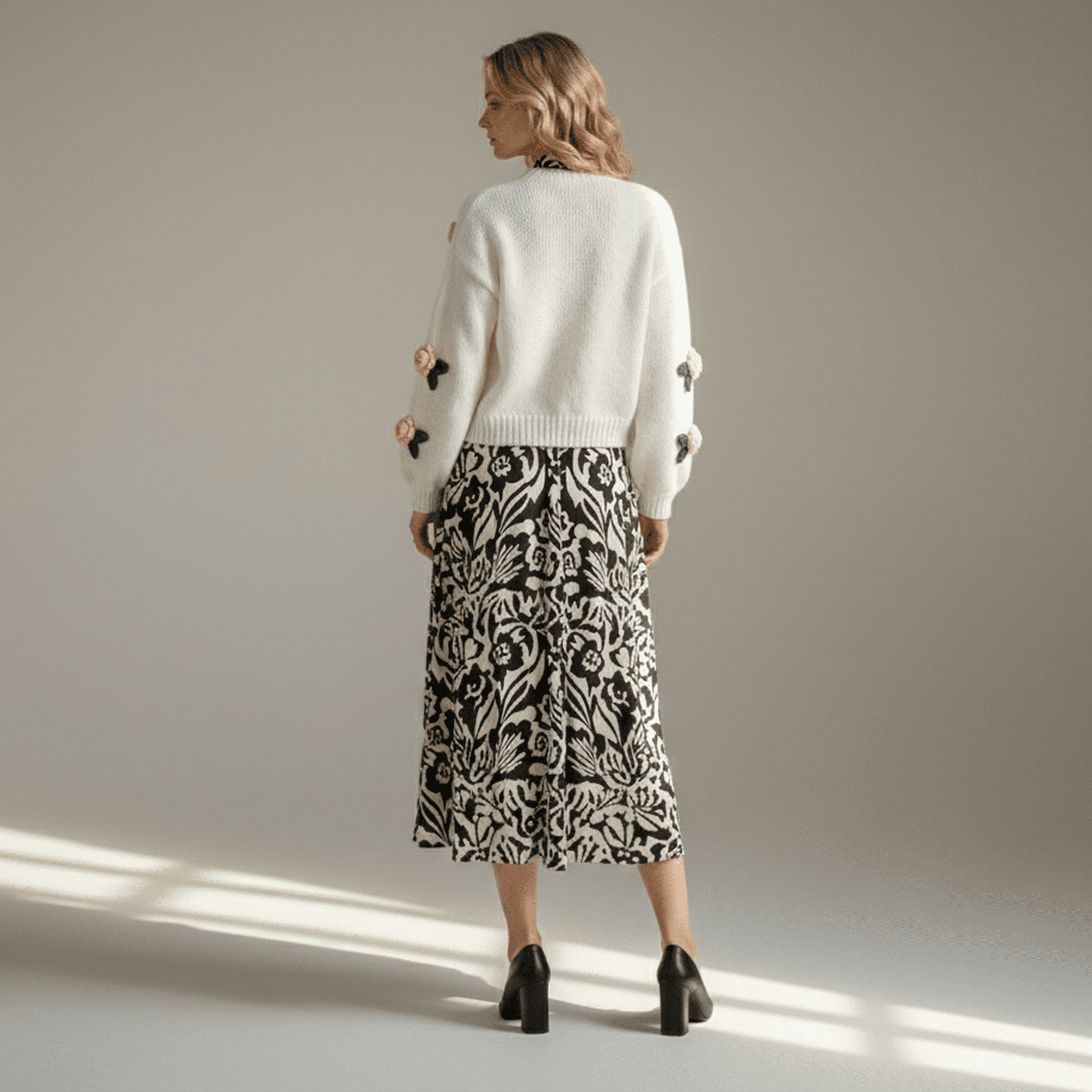 Woman wearing a white cardigan with floral embellishments and a patterned skirt on a beige background