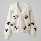 White cardigan with pink floral embellishments on a gray background