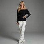 Woman wearing a black off-shoulder top and white pants on a gray background