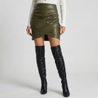 Person wearing a green leather skirt and black knee-high boots on a light gray background