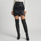 Person wearing a black leather skirt and knee-high boots on a light gray background