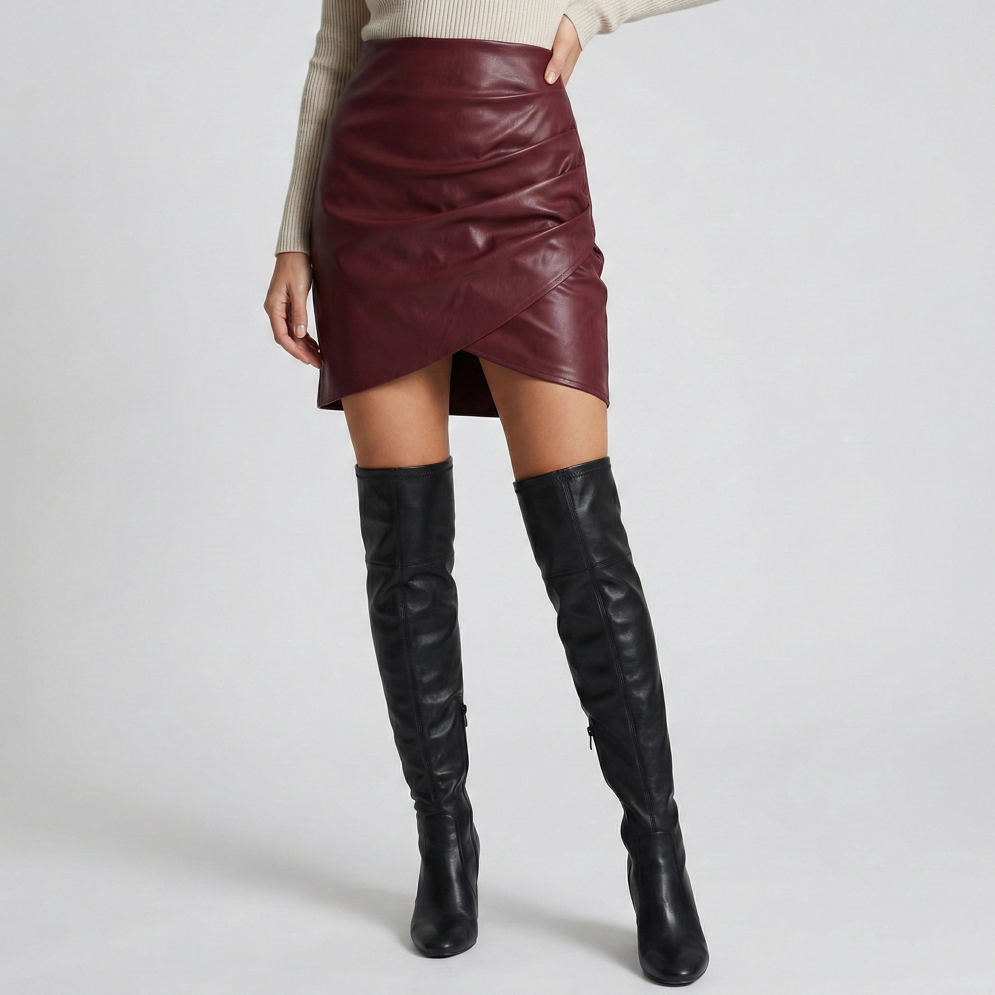 Person wearing a burgundy leather skirt and black knee-high boots on a light gray background
