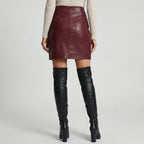 Maroon leather skirt worn with black knee-high boots on a plain background