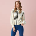Woman wearing a cream cardigan with black striped pattern and blue pants on a light gray background
