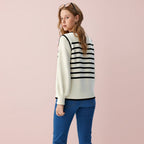 Person wearing a white sweater with black stripes and blue jeans on a light gray background