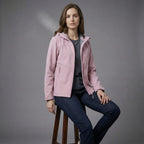 Woman wearing a pink jacket sitting on a stool against a gray background