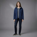 Person wearing a blue jacket and dark jeans on a gray background