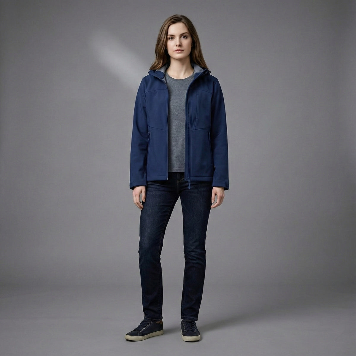 Person wearing a blue jacket and dark jeans on a gray background