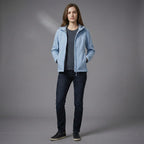 Person wearing a light blue jacket over a dark shirt with dark jeans on a gray background