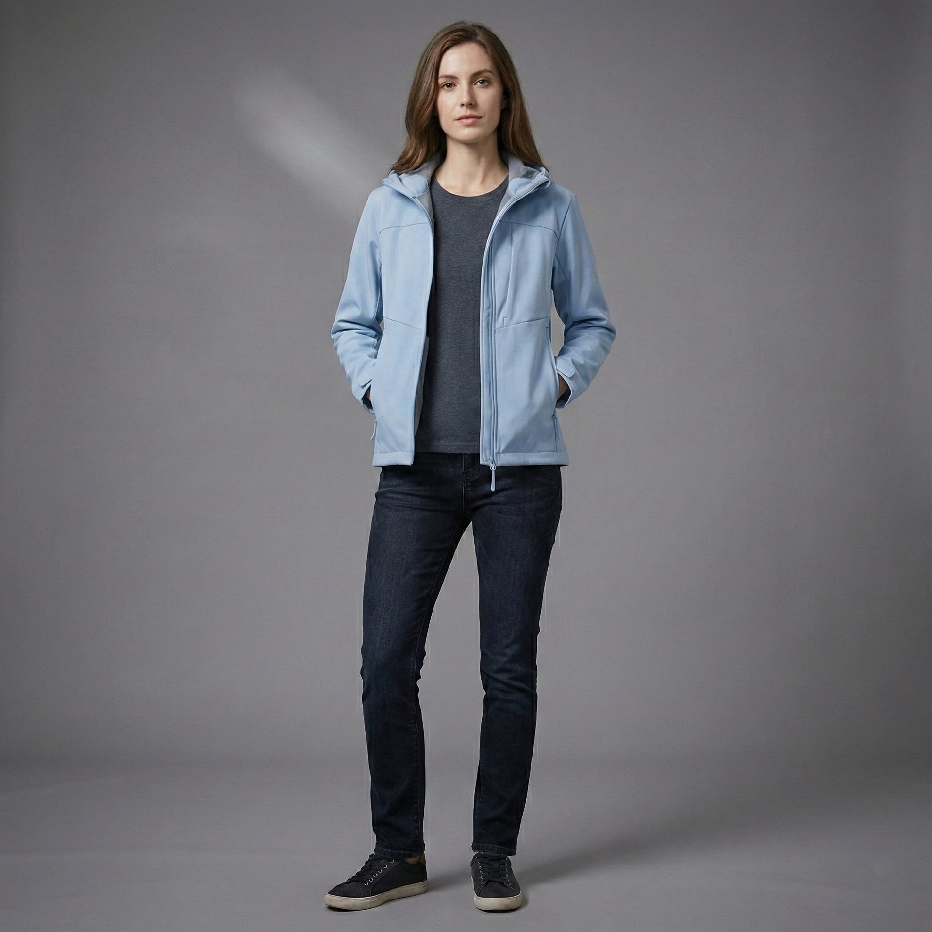 Person wearing a light blue jacket over a dark shirt with dark jeans on a gray background