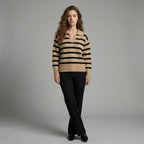 Woman wearing a beige and black striped sweater with black pants on a gray background