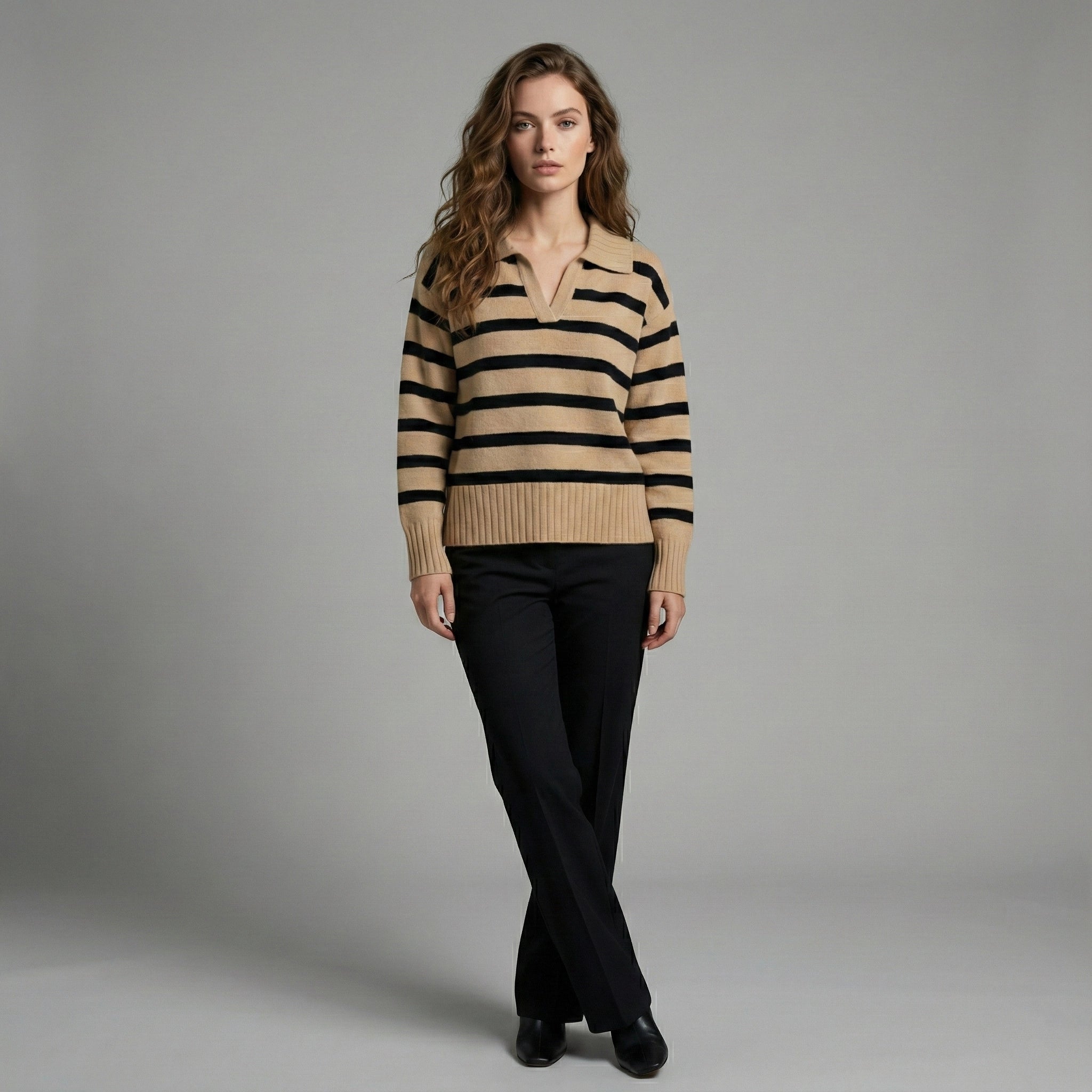 Woman wearing a beige and black striped sweater with black pants on a gray background
