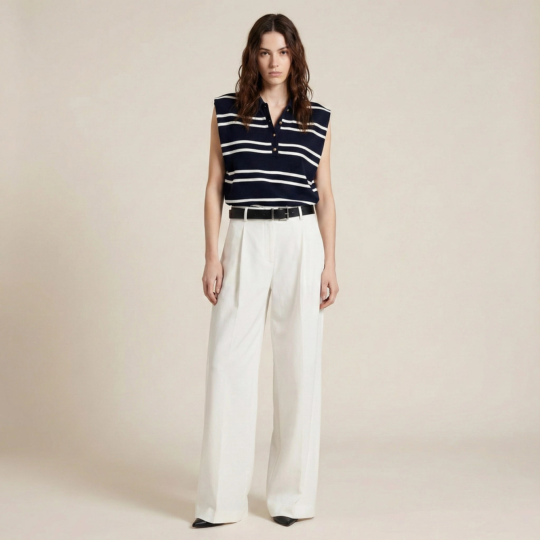 Woman wearing a sleeveless striped shirt and white pants on a beige background