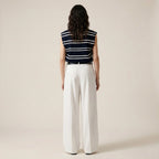 Person wearing a striped sleeveless top and white pants on a beige background